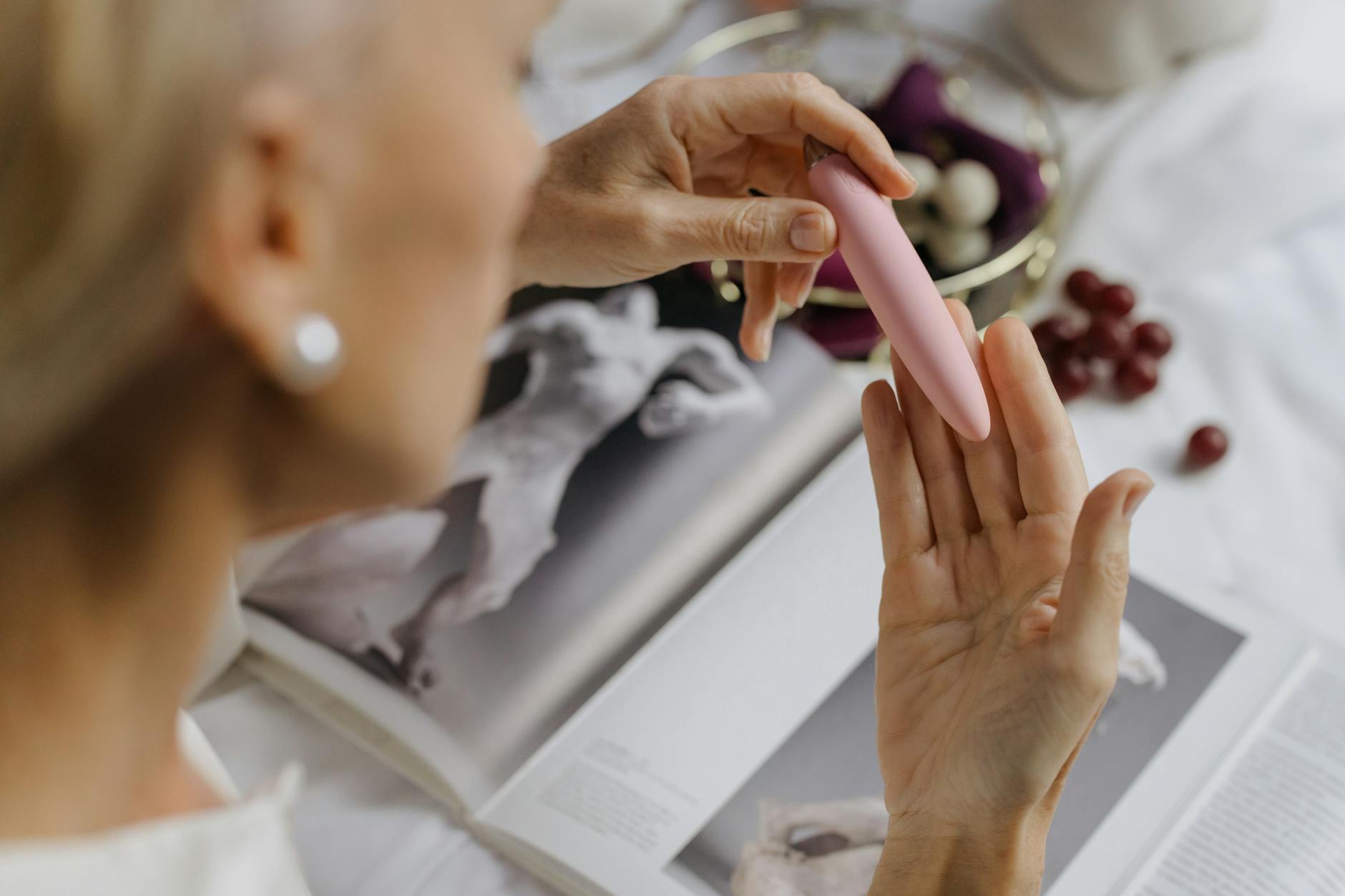 Close-up of hands holding a vibrator with art books in soft background, symbolizing intimacy and personal pleasure