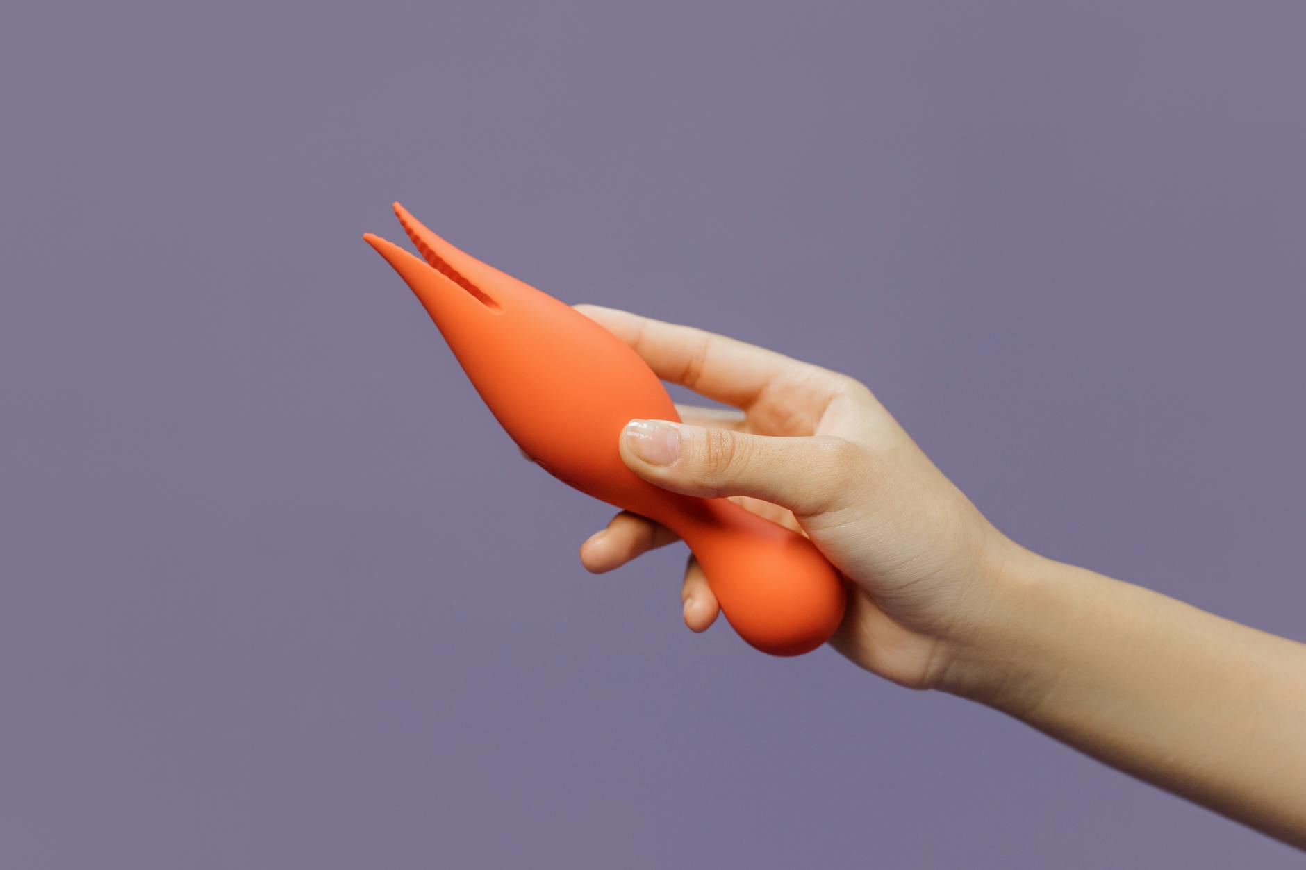 Close-up of a hand holding an orange vibrator against a minimalistic purple backdrop, symbolizing intimate reconnection.